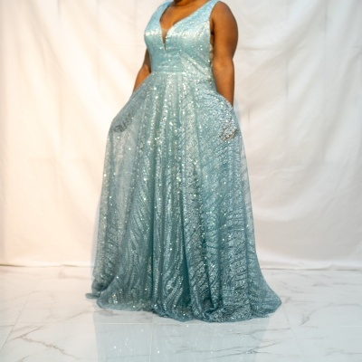 Vestido longo azul claro brilhante com padrão de lantejoulas num fundo branco e chão de azulejos