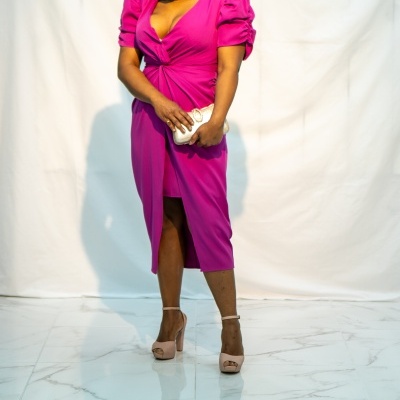 Mulher de vestido rosa fúcsia com clutch dourada em fundo branco