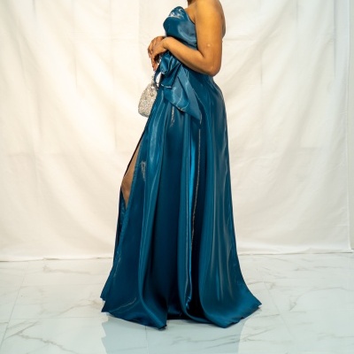 Mulher com vestido azul cetim longo e mala prateada, em fundo branco