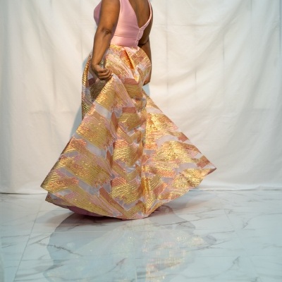 Mulher com vestido de festa rosa e dourado, fundo branco e chão de mármore.