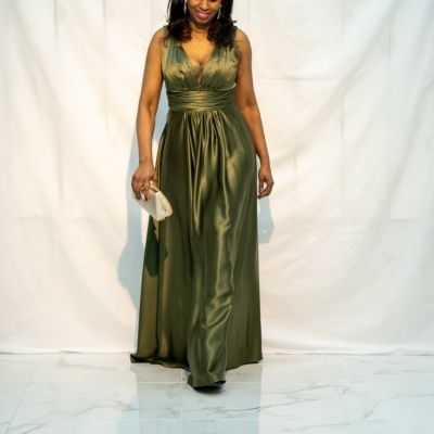 Mulher vestindo vestido longo verde oliva acetinado e segurando carteira bege