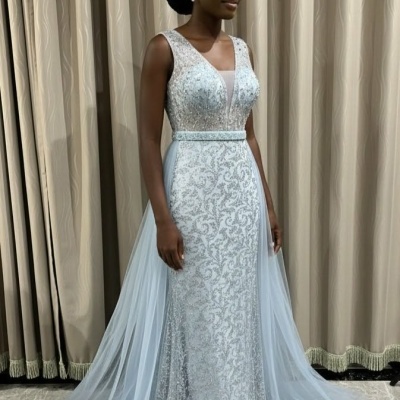 Vestido de festa prateado com padrão floral e tule azul claro ao fundo de cortinas bege