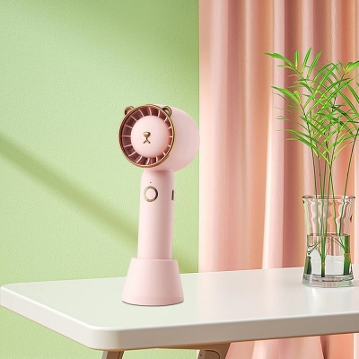 Ventoinha portátil rosa em forma de leão sobre mesa branca com planta ao lado
