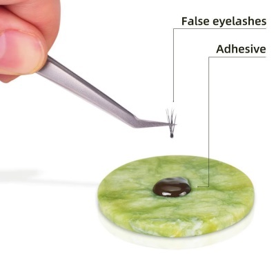 Pinça a segurar pestana falsa com adesivo sobre superfície verde marmoreada