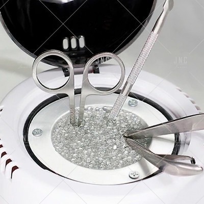 Instrumentos metálicos para manicure numa base branca com esferas translúcidas e tampa preta aberta