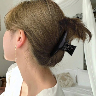 Presilha preta de cabelo em plástico brilhante segurando cabelo castanho claro