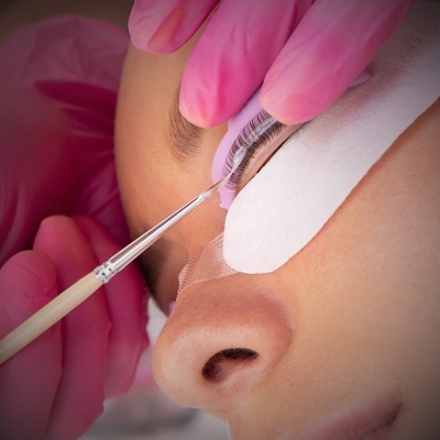 Aplicação de cola em extensão de pestanas com pincel e luvas rosas