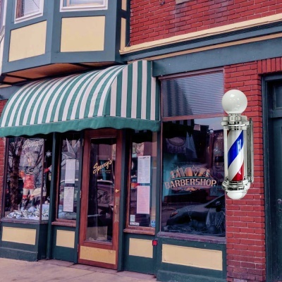 Fachada de barbearia com toldo riscado e poste luminoso de barbearia