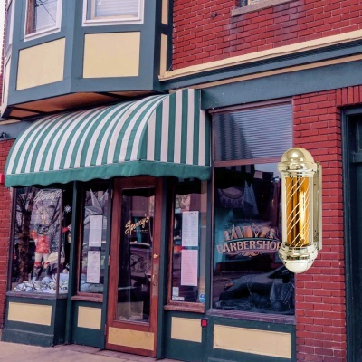 Fachada de barbearia com toldo verde e branco e lâmpada de barbeiro dourada
