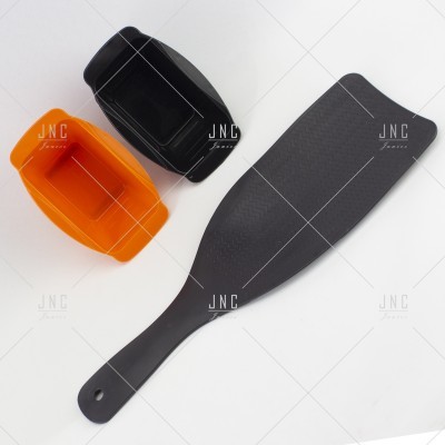 espátula preta e dois recipientes pequenos laranja e preto sobre fundo branco