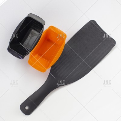 Espátula preta com cabo e dois pequenos recipientes nas cores preta e laranja