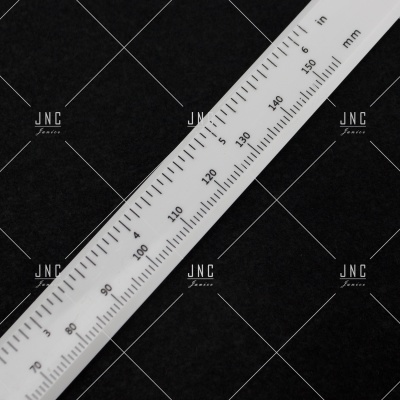 Régua branca de plástico com medidas em mm e polegadas sobre fundo preto