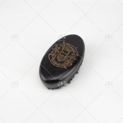 Escova oval preta com emblema dourado e cerdas preta sobre fundo branco.