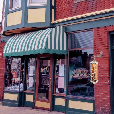 Fachada de barbearia com toldo verde e branco e lâmpada tradicional de barbearia