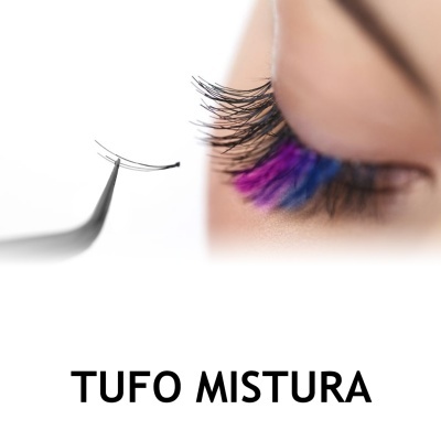 Tufo de pestanas falsas pretas segurado com pinça ao lado do olho com pestanas coloridas azul e roxo.