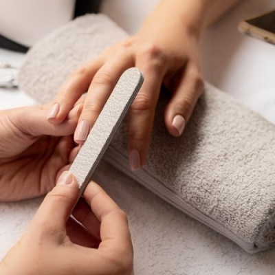 Pessoa a limar unhas de outra em sessão de manicure com toalha cinzenta na mesa