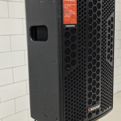 Coluna ativa preta V Sound Thunder com grelha hexagonal em pedestal preto em ambiente com azulejos brancos.