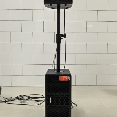 Sistema de som profissional preto com suporte, parede azulejos brancos.