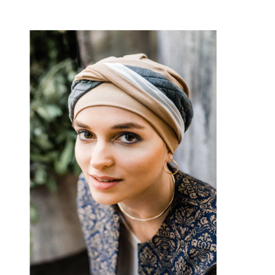 Mulher com turbante bege, cinza e branco e casaco azul escuro com padrão floral.