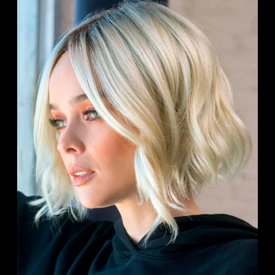 Mulher de perfil com cabelo loiro platinado ondulado e camisola preta com capuz