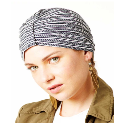 Mulher com turbante riscado preto e branco, casaco verde-oliva e brincos pendentes dourados.