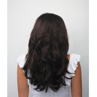 Mulher de costas com cabelo castanho ondulado e blusa branca de alças com folhos