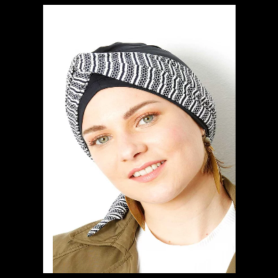 Mulher com turbante preto e branco de padrão geométrico, casaco verde e camiseta branca.