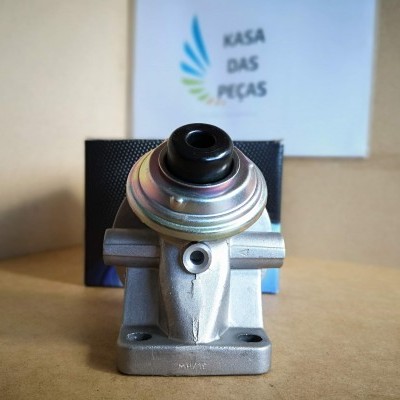 Peça mecânica prateada com componente preto em superfície castanha e placa com texto KASA DAS PEÇAS