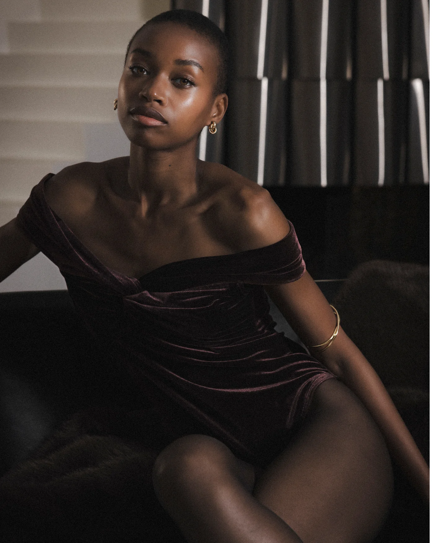 timeon body Mulher com body de veludo roxo escuro e joias douradas sentada em ambiente interior