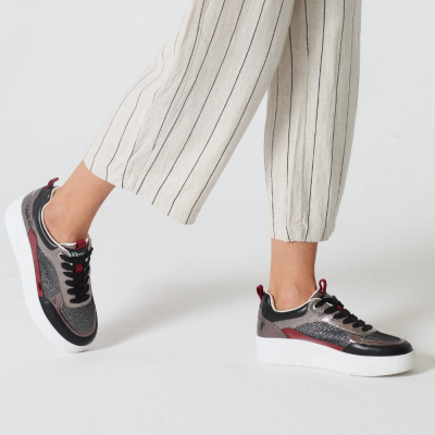 Ténis pretos cinzentos com detalhes vermelhos e sola branca usados com calças bege às riscas