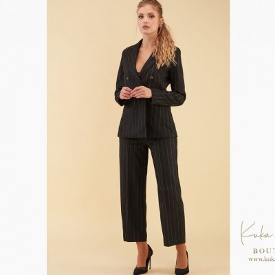 Mulher a usar conjunto preto com riscas brancas finas, blazer e calças, sapatos pretos, fundo bege e logótipo Kuka Pazza Boutique