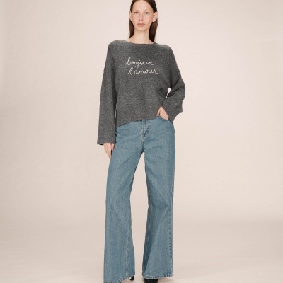 Mulher vestindo camisola cinza escura com texto branco e calças de ganga azul