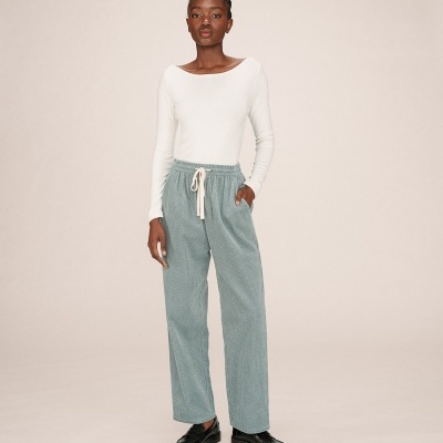 Mulher a usar calças largas cinza-azul com cordão branco e camisola branca de manga comprida.