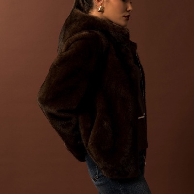 Mulher de perfil com casaco castanho de pelo, brincos dourados e jeans azuis