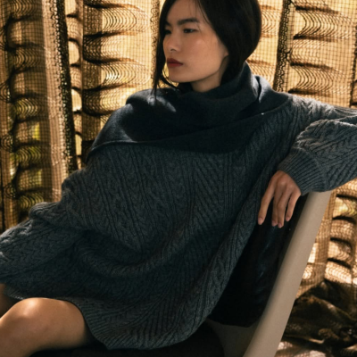 Mulher sentada numa cadeira bege vestindo vestido de malha cinzento escuro com padrão de trança