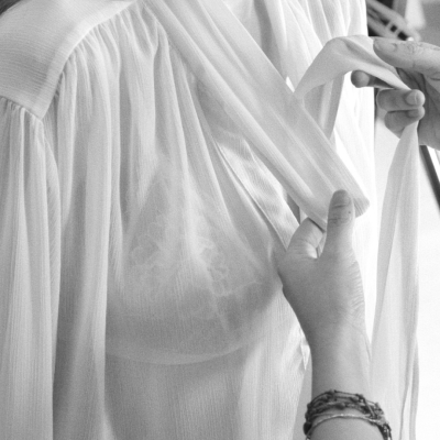 Blusa branca feminina transparente com detalhe franzido e mãos ajustando o decote