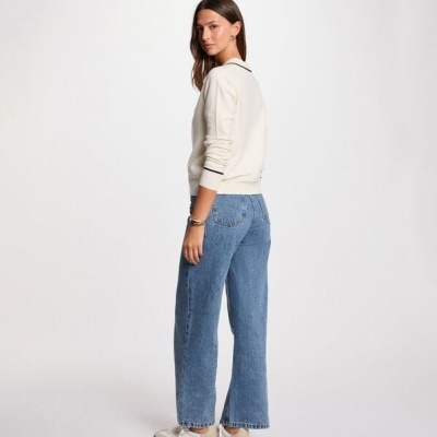 Mulher com jersey branco, jeans azuis e sapatilhas brancas em fundo branco