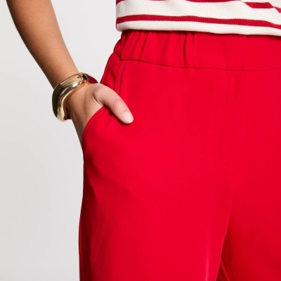 Calças vermelhas com cintura elástica e bolso, pulseira dourada e camisola riscada de vermelho e branco