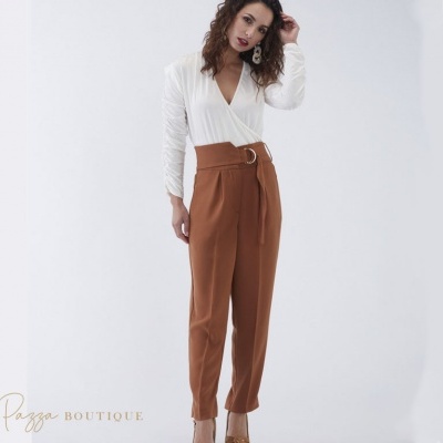 Mulher veste blusa branca e calças castanho-escuro com cinto numa foto com fundo branco