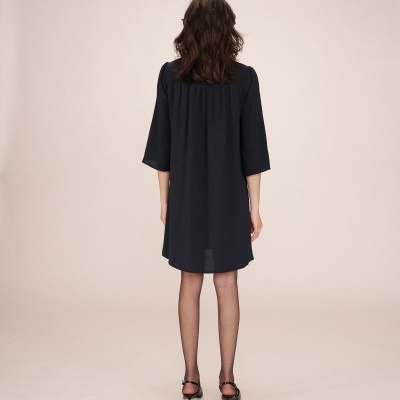 Mulher de costas a usar vestido azul escuro, meia preta e sandálias pretas