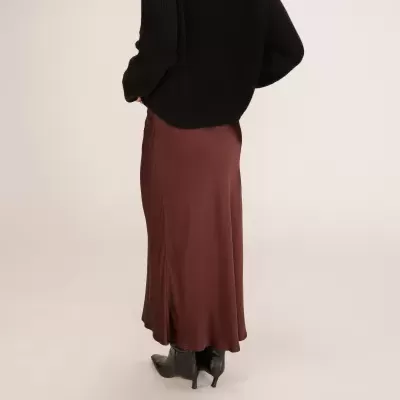 Saia comprida castanha satinada com camisola preta e botas pretas vista de costas