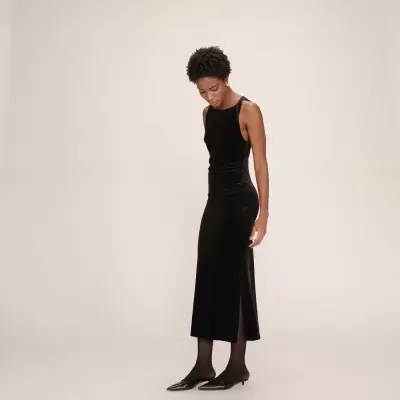 Mulher com vestido preto longo de veludo, meias pretas e sapatos pretos de salto baixo.