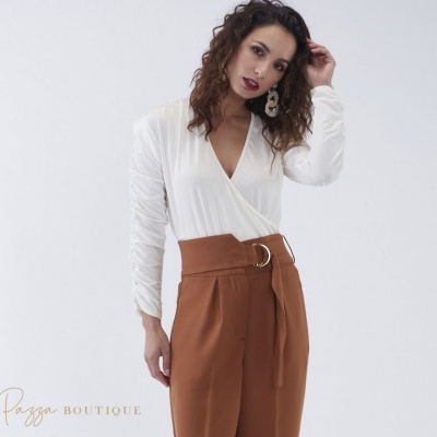 Mulher com calças castanhas e camisa branca em fundo branco com texto Kaka Pazza BOUTIQUE