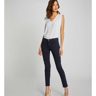 Mulher com camisa branca de decote em V e calças pretas, calçada com sandálias brancas de tiras.