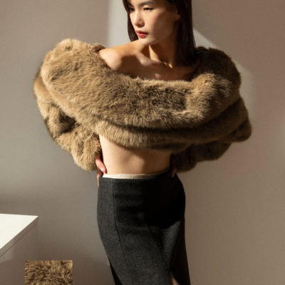 Mulher usando casaco curto de pelo sintético castanho sobre os ombros e saia preta longa com racha revela renda creme.