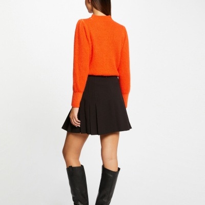 Mulher de costas com camisola laranja, saia preta e botas pretas altas