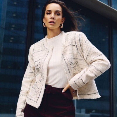 Mulher a usar casaco branco de malha com padrão de estrelas e calças bordô em cenário urbano