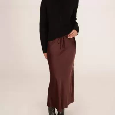 Vestido castanho comprido em tecido acetinado com cordão, camisola preta de gola alta em malha e botas pretas.