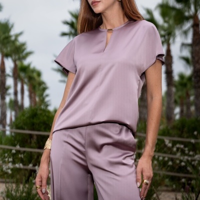 Conjunto feminino lilás acetinado com blusa e calças em ambiente exterior com palmeiras.