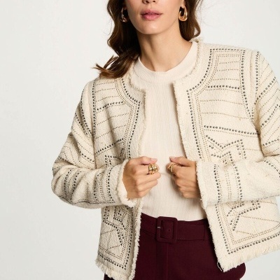 Blazer creme com padrão geométrico e franjas, usado com camisola creme e calças bordô cintadas.